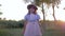 Child girl in sunglasses and straw hat dancing at the camera at sunset in the village