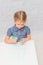 Child, a girl at the table writes, draws on a piece of paper, against a white brick wall