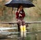 Child girl with umbrella sits on wooden bridge and laughes in ra