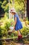 Child girl watering flowers in summer garden, little helper