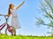 Child girl wearing white skirt rides bicycle into park.