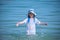 Child girl in wet white dress and big hat standing in ocean water enjoying summer vacations