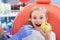 Child girl in white clothes at reception at a pediatric dentist smiles and laughs. little girl bites a big green apple with her