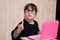 The child in glasses and old clothes is sitting at the laptop. Shows gesture thumbs up