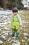 Child in green thermal clothing playing in the snow in the forest