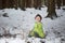 Child in green thermal clothing playing in the snow in the forest