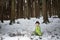 Child in green thermal clothing playing in the snow in the forest