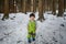 Child in green thermal clothing playing in the snow in the forest