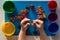 Child hand holding multicolored toys to separating into colorful cups by color on the blue surface