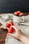 Child hand holding strawberry, sugar and cup of strawberries on linen cloth and rustic wooden background. Summer healthy eating
