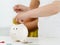 Child hand putting pin money coins into white piggybank slot