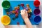 Child hand separating by color multicolored toy stones scattered on the blue surface into colorful cups