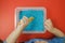 Child hands playing yellow spoon with blue colored rice in the sensory box. Baby`s sensory educational kit