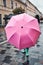 Child hiding behind big pink umbrella walking in a downtown on rainy gloomy autumn day