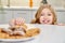 Child hiding and taking biscuits with raisins from table.