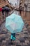 Child holding big blue umbrella walking in a downtown on rainy gloomy autumn day