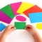 Child holds green cardboard rectangle in hands and looking for corresponding color card.Kid learns colors and form with paper card