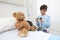 Child in hospital room playing with a sphygmomanometer and a teddy bear imitating doctor