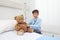 Child in hospital room playing with a stethoscope and a teddy bear imitating doctor