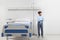 Child in hospital room standing next to bed wearing a pajama isolated on white wall