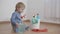 Child with household chemicals sitting near a bucket with plastic bottles, kid boy sprays detergent on rubber glove and