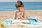 Child immersed in reading a book on the towel on the beach on a sunny day