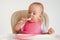 The child independently eats cottage cheese with a spoon while sitting on a chair