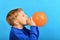 The child inflates an orange balloon on a blue background