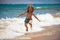 Child jumping on ocean beach. Kid jump in the waves at sea vacation. Little boy running on tropical beach of exotic