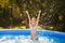 The child jumps out of the water. A girl splashes in an inflatable pool in the garden on a sunny summer day