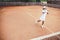 Child learning to play tennis in the sport club. Full length shot of a little girl tennis player on clay court. Sporty child girl