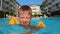 child learning to swim, water safety, little boy with yellow inflatable oversleeves swims in pool outdoors