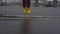 Child legs in yellow rubber boots dance and jump in puddle