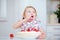 Child licks cream from finger while eating cake