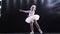 Child Little ballerina in pink tutu dancing on the stage. Happy child. Smiles. In the backlight. Slow motion