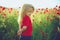 Child with long blonde hair in red shirt in flower field of poppy. spring kids, childhood and happiness.