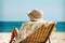 child lying on a beach lounger on sand, covered with a towel and with a panama on his head, ocean and sky background. Generative