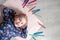 Child lying on the floor paper looking at the camera near crayons. Little girl painting, drawing. Top view. Creativity concept.