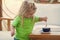 Child is making coffee for his mother. Child boy with blond long hair mixing sugar with teaspoon.