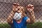 Child in medical mask behind a fence on the street. Covid-19 coronavirus pandemic, virus protection