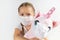 Child in medical mask hugs a soft pink masked unicorn on a white background