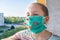 A child in a medical mask looks at an empty street near the house .