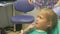 Child with a mother at a dentist`s reception. The girl lies in the chair, behind her mother. The doctor works with an