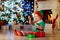 Child opening present at Christmas tree at home. Kid in elf costume with Xmas gifts and toys. Little baby boy with gift box and