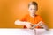 Child in an orange T-shirt sits at a table and twists thin paper strips on a quilling tool