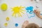 The child paints the yellow sun and blue clouds at a white table. Top view on a white table, paints, hands of a child