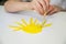 A child paints a yellow sun at a white table