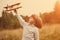 Child pilot aviator with plane at sunset, little boy playing with cardboard toy airplane outdoors, against summer sky background.