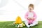 Child in pink fluffy costume sitting near yellow ostrich egg, colorful chicken eggs and tulips isolated on white