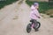 Child in pink jacket and lilac hat rides balance bike on dirt road, in countryside